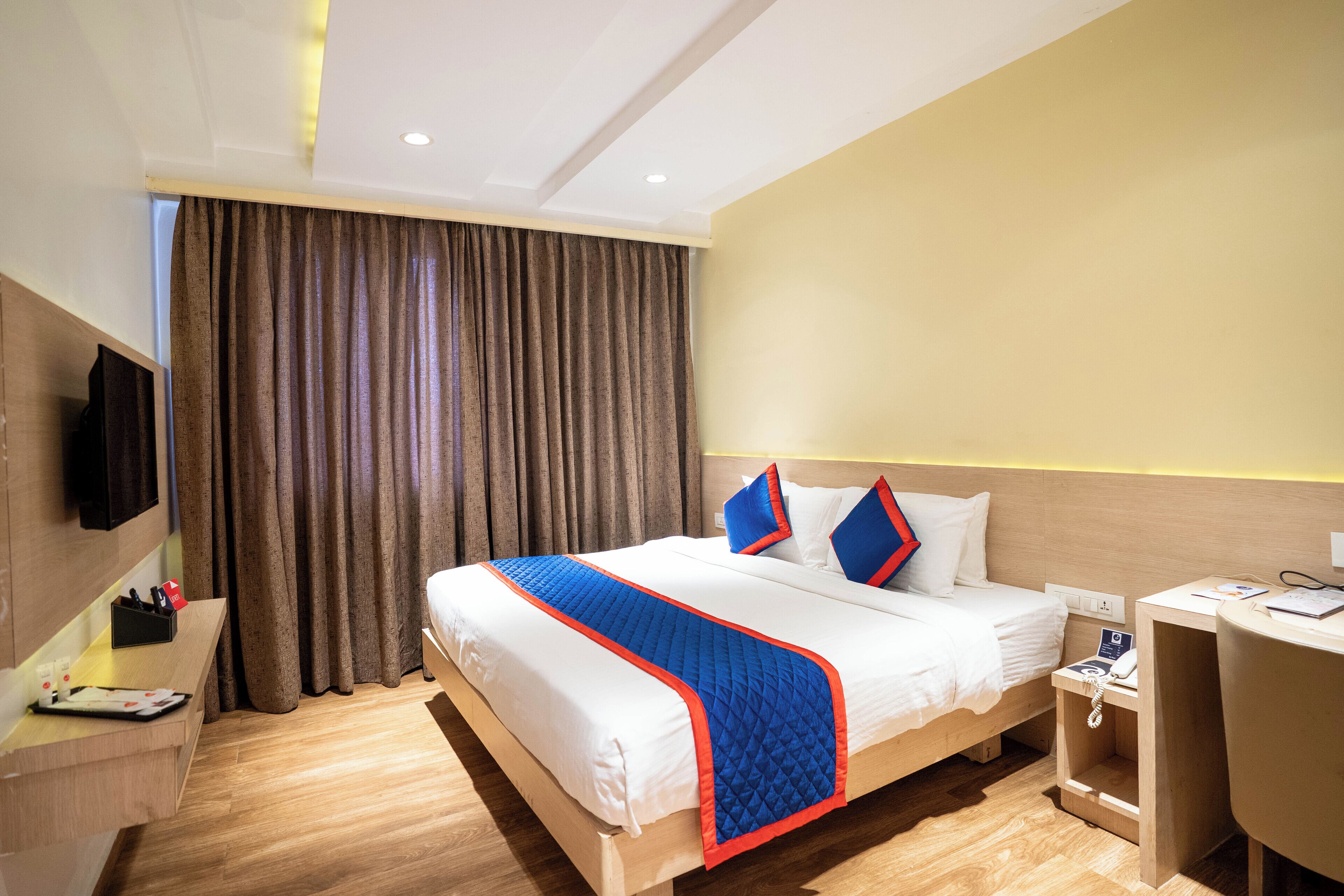 A hotel room with a bed, bedside table, desk, and a television.
