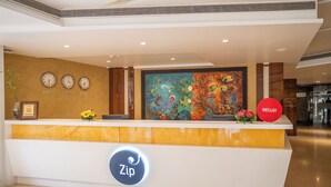 A hotel reception desk with clocks displaying New York, Mumbai, and Tokyo times, a colorful mural, and a 'Zip' logo. - Zip By Spree Hotels Samudra (Belagavi)