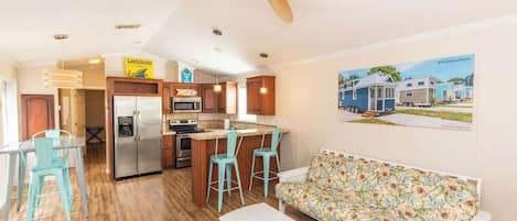 Een moderne keuken met een centraal eiland, een eetgedeelte met een tafel en stoelen, en een zithoek met een bank en een aan de muur bevestigde televisie.