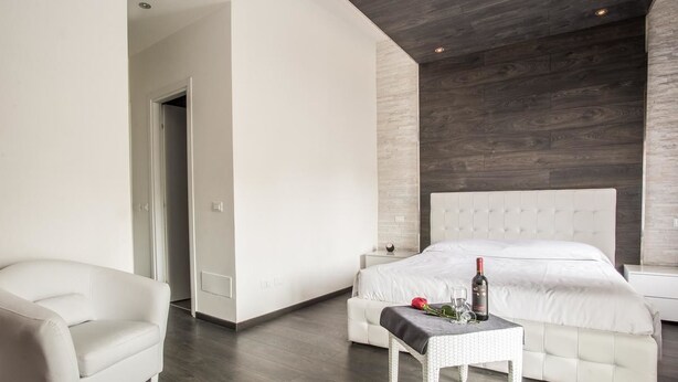 A modern bedroom with a large bed, a white sofa, and a small table with a bottle and glasses. - Royal Rooms Colosseo (Rome)