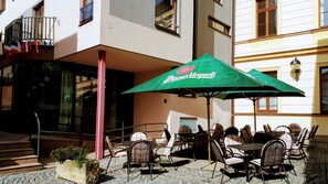 Relax on the cobblestone-paved terrace with tables and chairs, surrounded by green umbrellas and a potted plant.