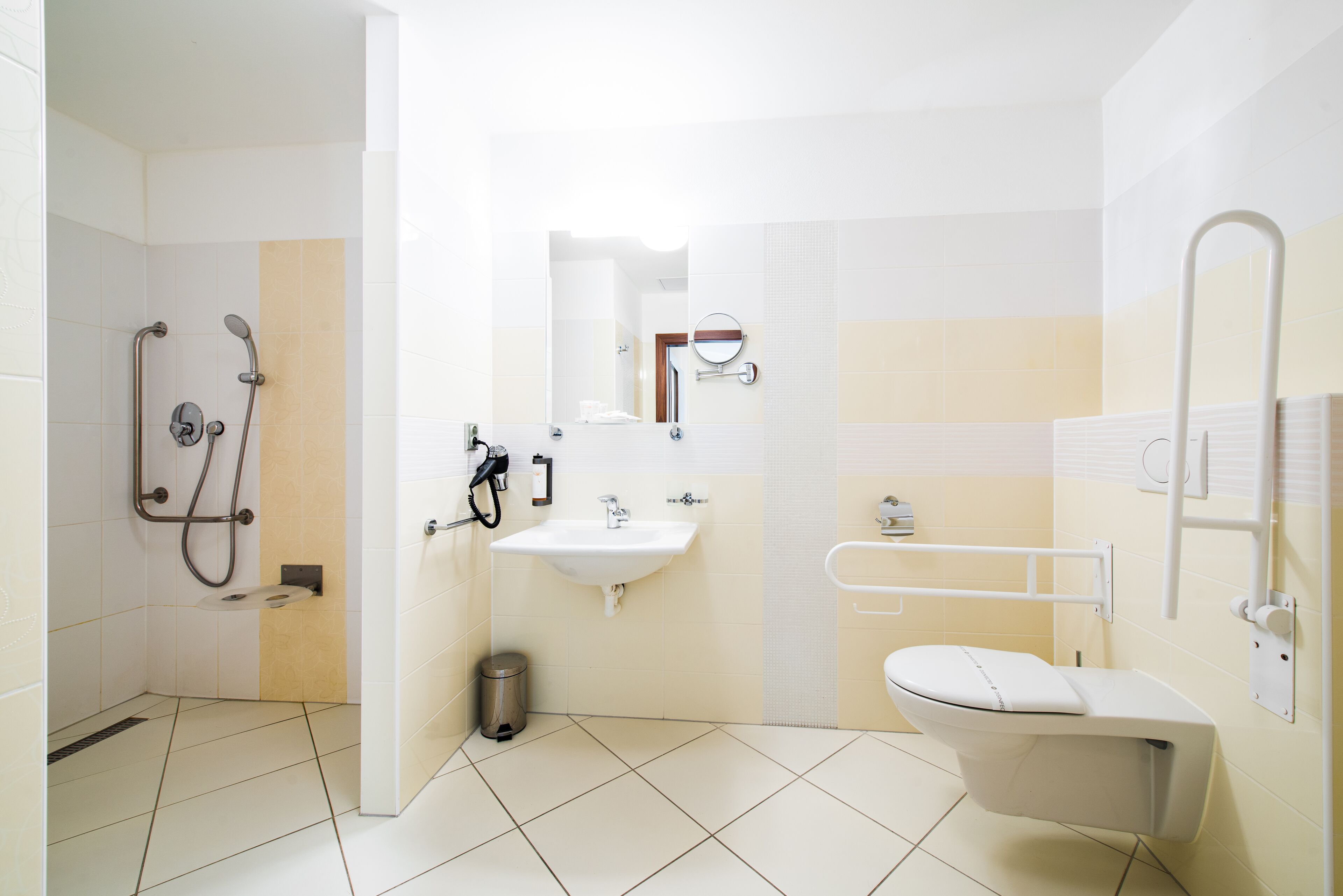 A bathroom with a shower, sink, toilet, and grab bars.