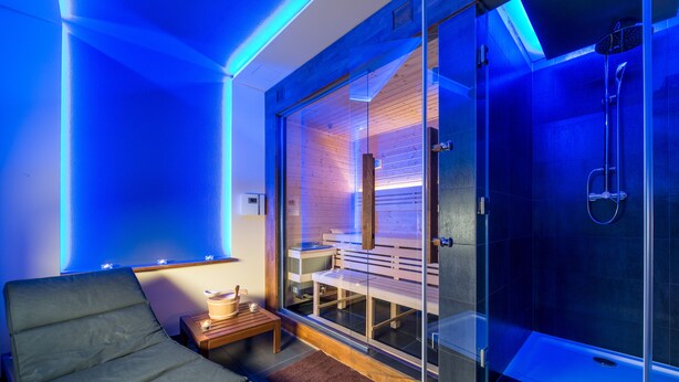 Un moderno spa con sauna de vidrio, zona de relajación con camilla de masaje y banco de madera.