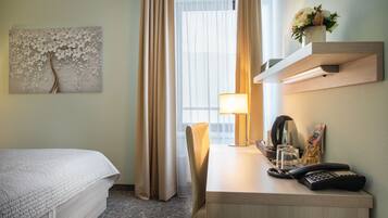 Een hotelkamer met een bed, een bureau met een lamp, een telefoon en een wandplank met een bloevas.