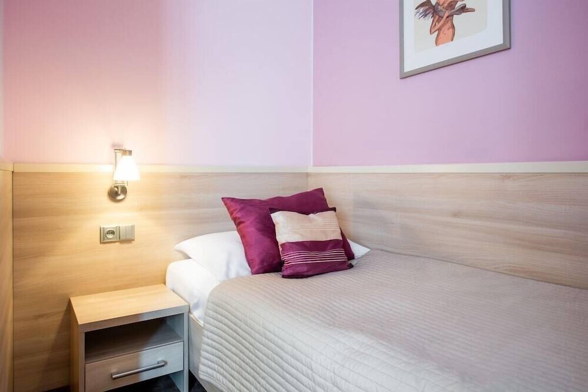 Una habitación de hotel con cabecera de madera, una mesita de noche con lámpara, cama con cubrecama acolchado y un cuadro en la pared.