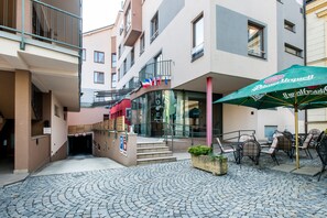 Enter through the glass entrance and discover a charming urban oasis with a cobblestone courtyard, outdoor seating, and a staircase leading up to the entrance.
