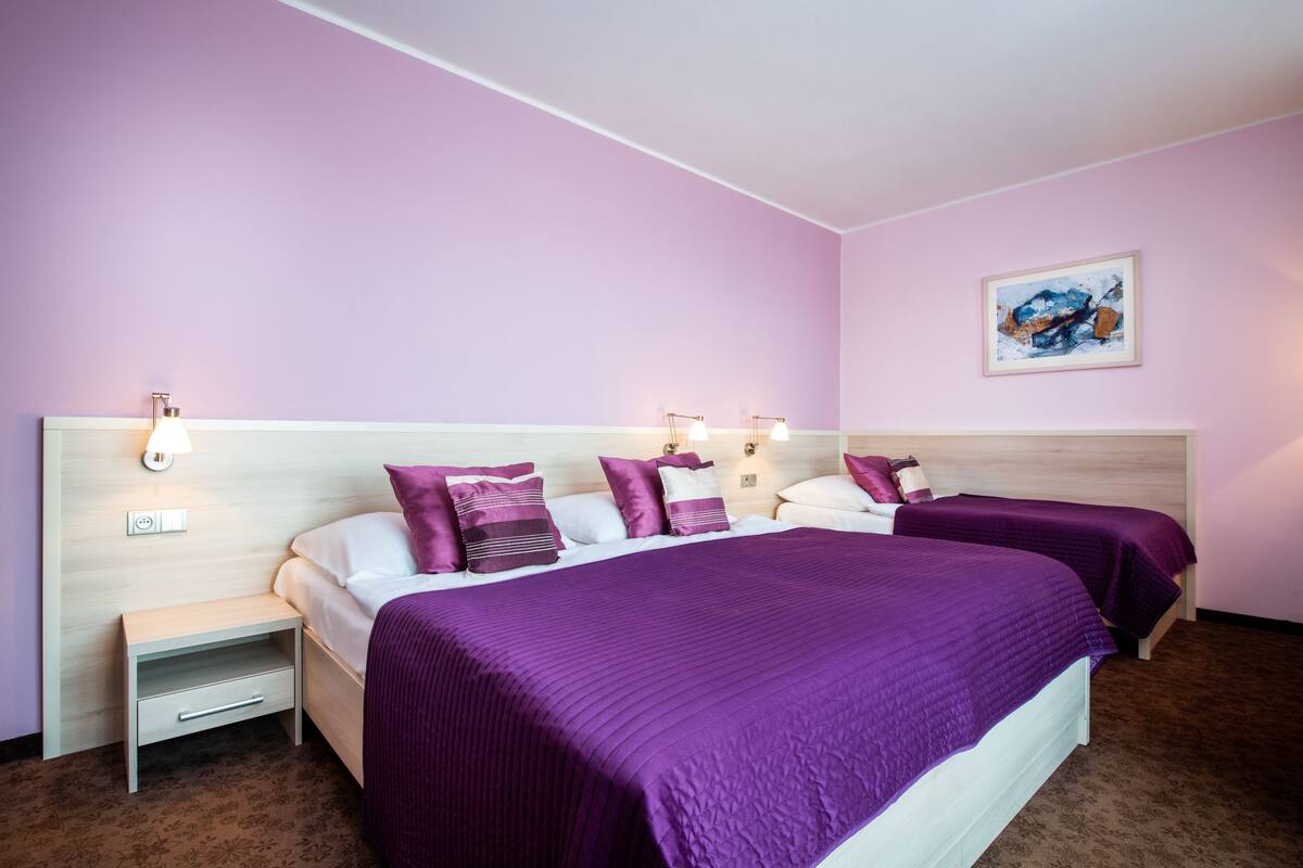 Habitación de hotel con dos camas, una mesita de noche y una lámpara fijada en la pared.