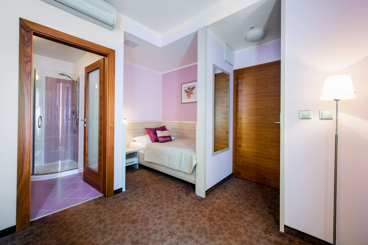 Habitación de hotel con ducha, cama con almohada rosa, puerta de madera y una lámpara.