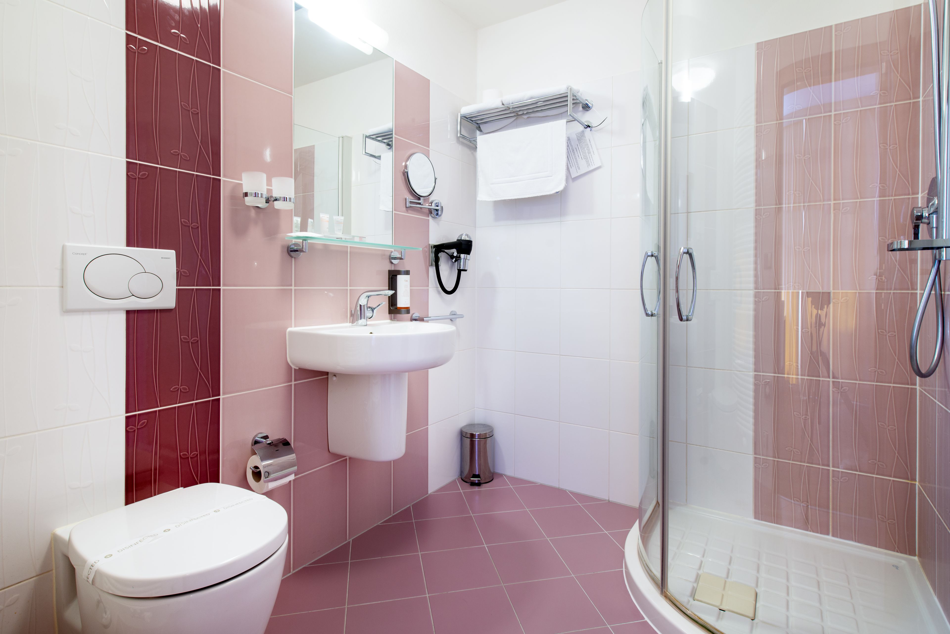 A modern bathroom with a toilet, sink, mirror, towel rack, and shower.