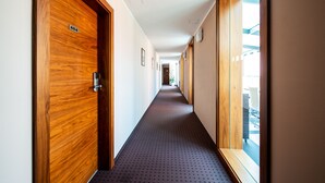 Un pasillo con puertas de madera, suelo alfombrado y vista a un edificio exterior.