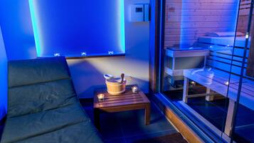 A modern room with a sofa, a wooden table with a bowl and spoon, and a glass partition with a bed and shelves.
