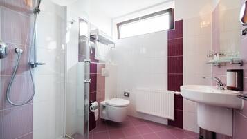 A modern bathroom with a glass-enclosed shower, a white toilet, a white sink, and a window above the toilet.