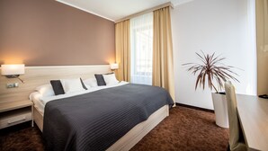 Habitación de hotel con una cama grande, lámparas de noche, una planta en maceta y vistas al exterior.