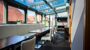 Un restaurante moderno con techo de cristal, asientos blancos acolchados y vistas de los edificios de tejados rojos al exterior.