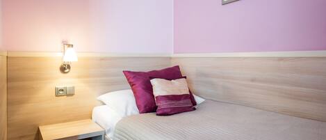 A neatly made bed with a headboard, a bedside table with a lamp, and a wall-mounted light fixture.