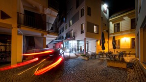 Una calle empedrada con un coche pasando, edificios con balcones y terrazas al aire libre.
