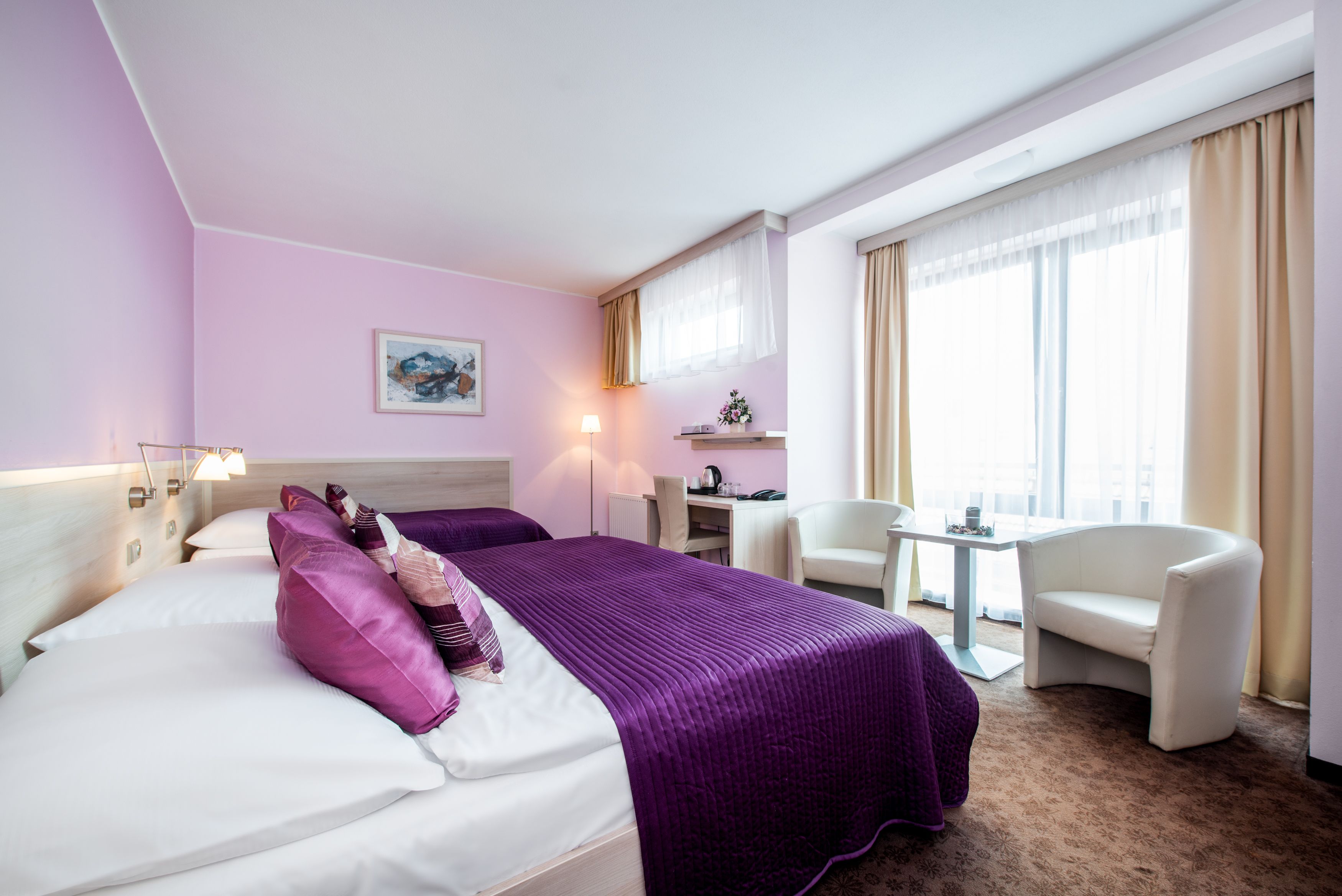 Habitación de hotel con cama, dos sillas, escritorio y ventana con cortinas.