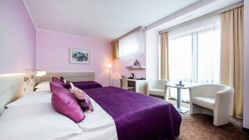 Habitación de hotel con cama, dos sillas, escritorio y ventana con cortinas.