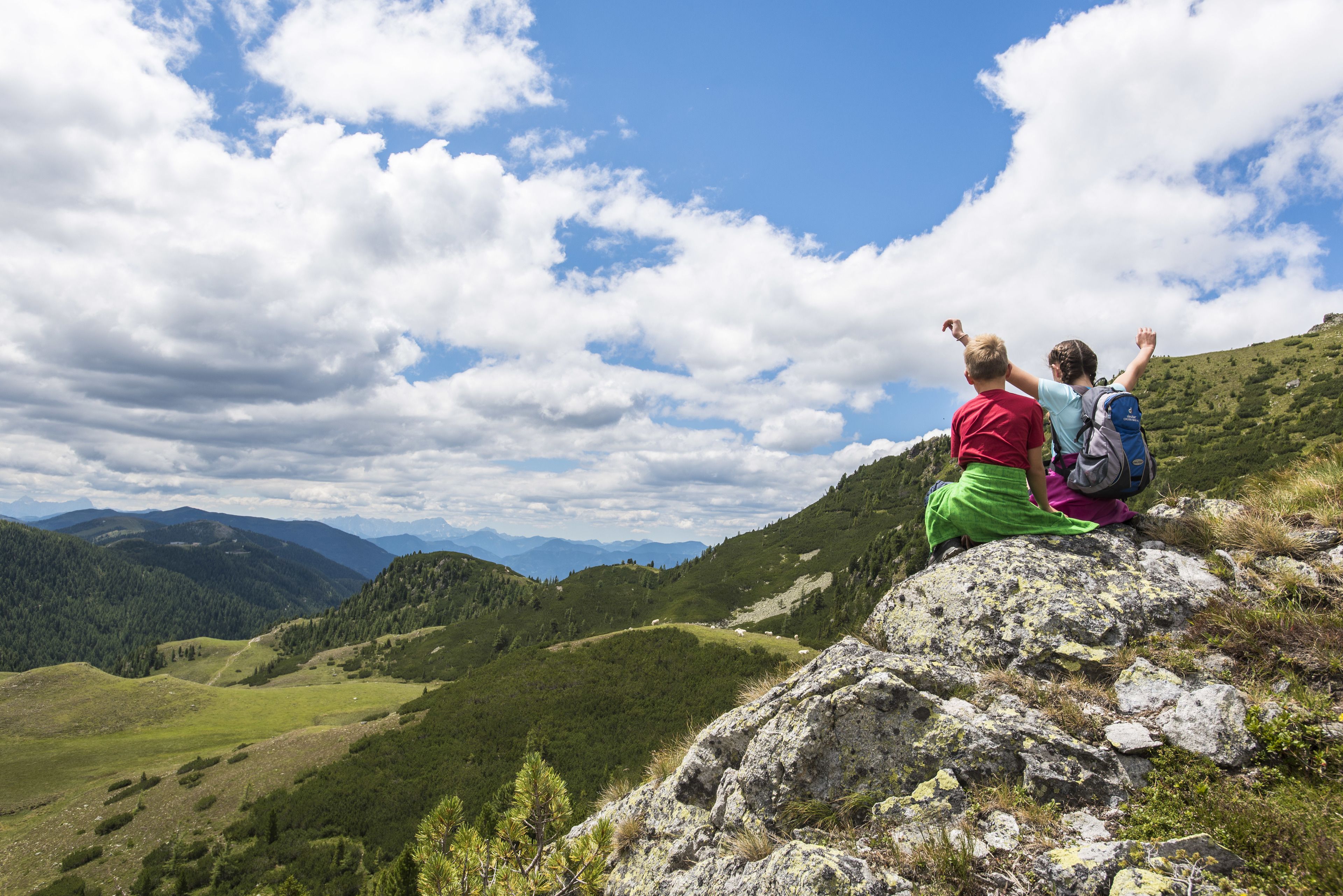 Two people sitting on a rocky outcrop overlooking a mountainous landscape.