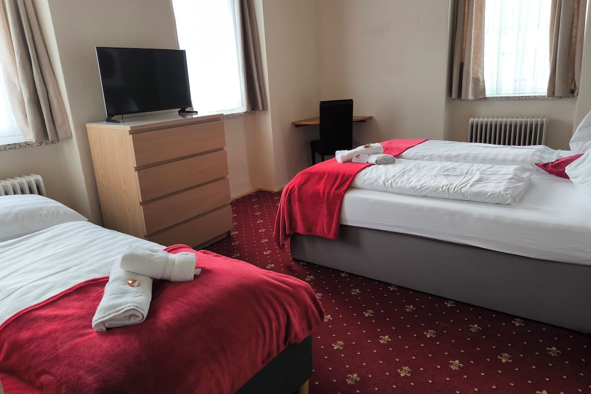Une chambre d’hôtel avec deux lits, un téléviseur posé sur une commode et une moquette rouge.
