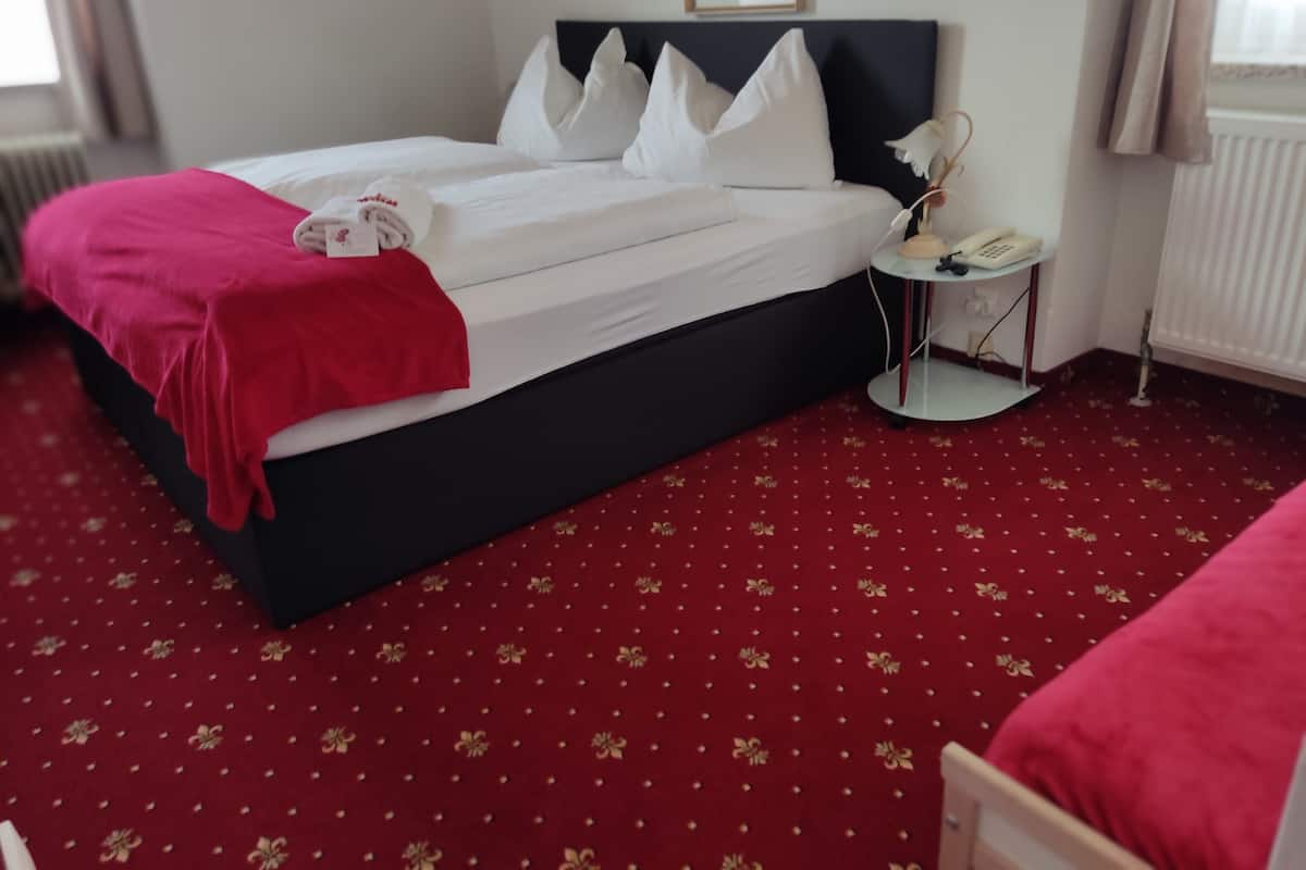 Une chambre d’hôtel avec un lit, une table de chevet avec une lampe et une moquette rouge.
