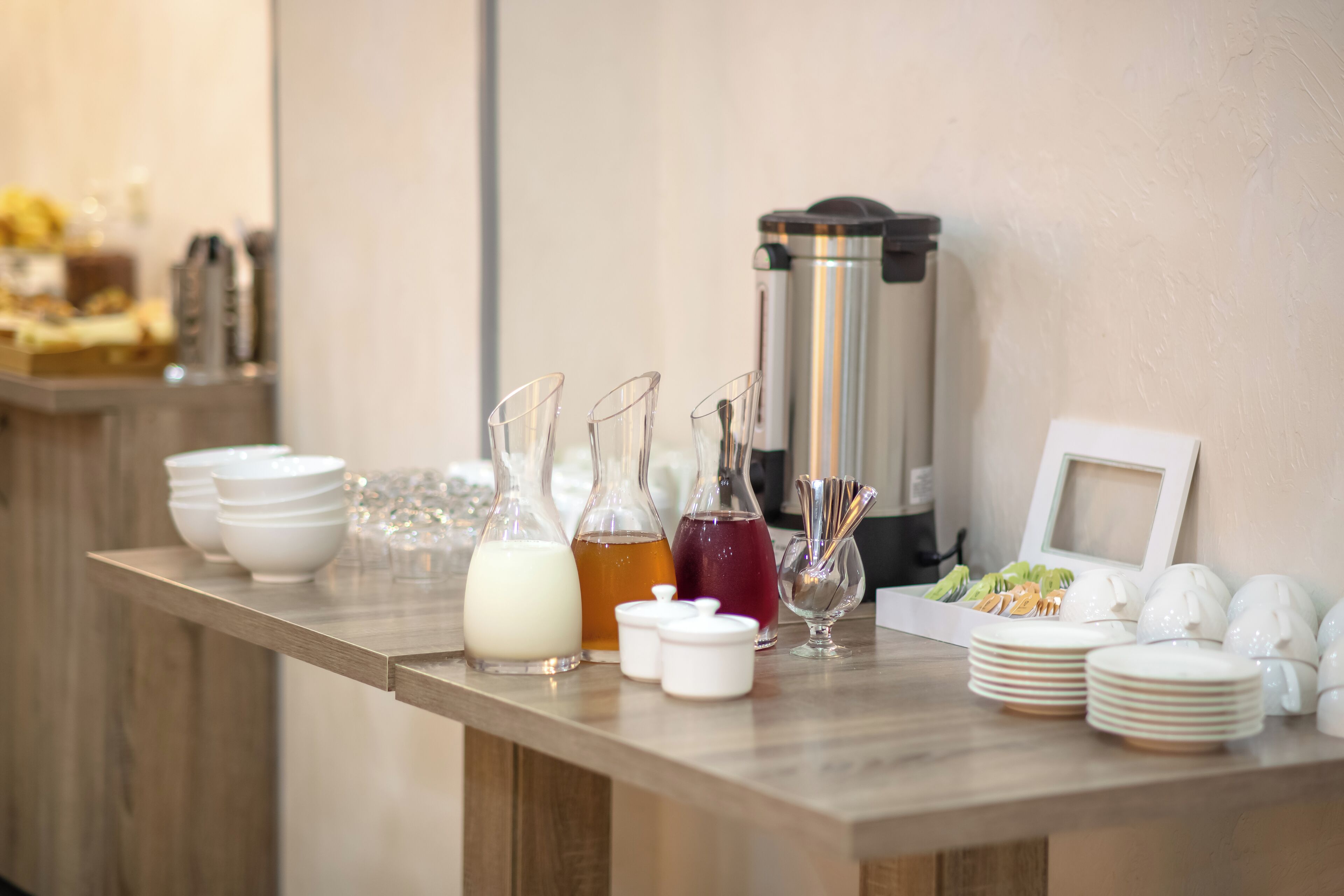 Un montaje de buffet con diferentes recipientes de comida y bebida, una cafetera y platos apilados.