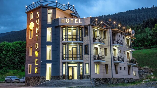Un hôtel à plusieurs étages doté d’un balcon au deuxième étage, d’une base en pierre et d’une enseigne indiquant « SUNTOWER HOTEL ».