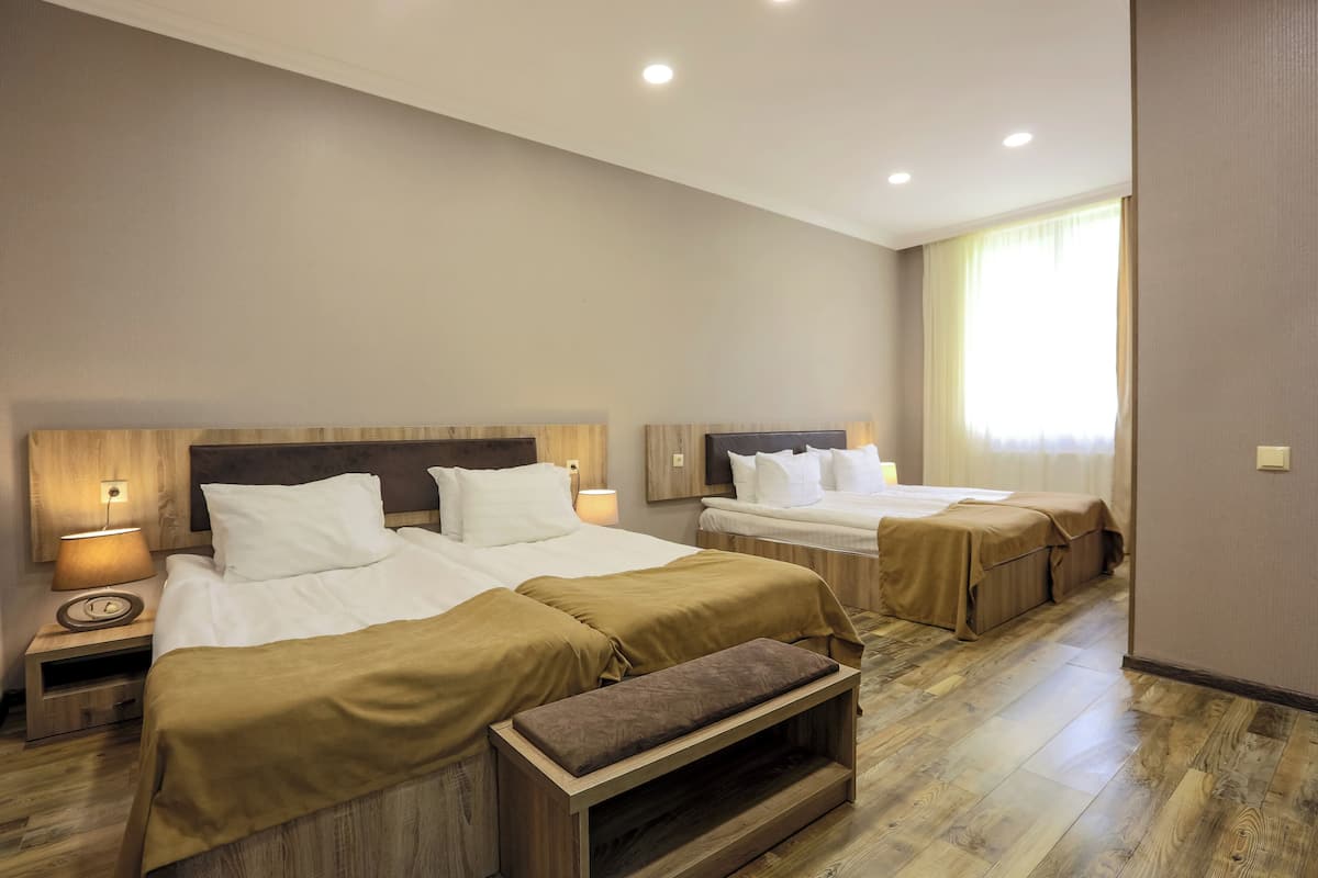 A hotel room with two beds, a bench, a nightstand with a lamp, and a large window.