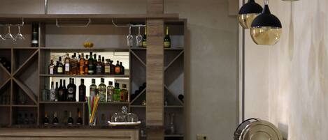 A bar area with wooden shelves stocked with bottles and glasses, and pendant lighting.