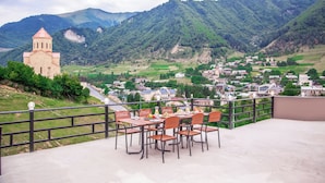 Une terrasse avec des tables et des chaises, d’où l’on a vue sur un village et des montagnes.