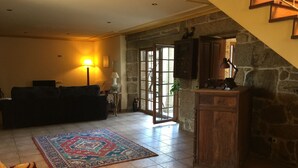 A living room with a sofa, a patterned rug, a wooden cabinet, and a staircase with a stone wall. - O Candil De Santa Ana (Ponte Caldelas)