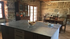 A kitchen with a granite countertop, a stone wall, and a dining area with wooden furniture. - O Candil De Santa Ana (Ponte Caldelas)
