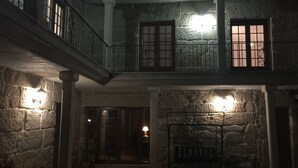 A stone building with a balcony, a bench, and a door leading to an interior space. - O Candil De Santa Ana (Ponte Caldelas)