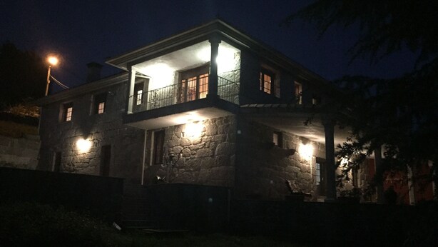 A two-story stone building with a balcony on the upper floor, illuminated by exterior lights. - O Candil De Santa Ana (Ponte Caldelas)