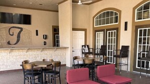 A spacious outdoor patio with wicker furniture, ceiling fans, and a large wall-mounted TV. - Gorgeous Condo in Prestigious Championsgate Golf Resort Community w View of Pool (Championsgate)