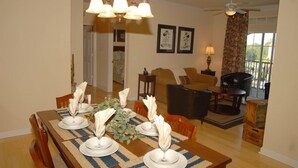 A dining area with a wooden table set for four, a chandelier, and a view of the living room in the background. - Gorgeous Condo in Prestigious Championsgate Golf Resort Community w View of Pool (Championsgate)
