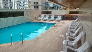 Piscina com deck revestido, espreguiçadeiras e área coberta com telhado.