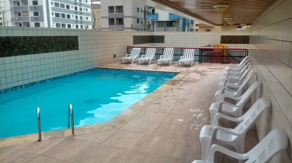 A swimming pool with a tiled deck, lounge chairs, and a covered area with a roof.
