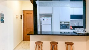 Uma cozinha moderna com armários brancos, bancada preta e três cadeiras de madeira.