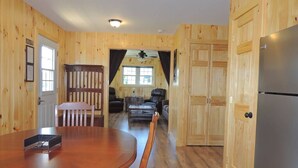 Un interior de madera con una mesa de comedor, sillas, un refrigerador y una zona de estar con sofás y una mesa de centro.
