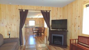 Un salón con paneles de madera, una mesa de centro de vidrio, un televisor y una chimenea.