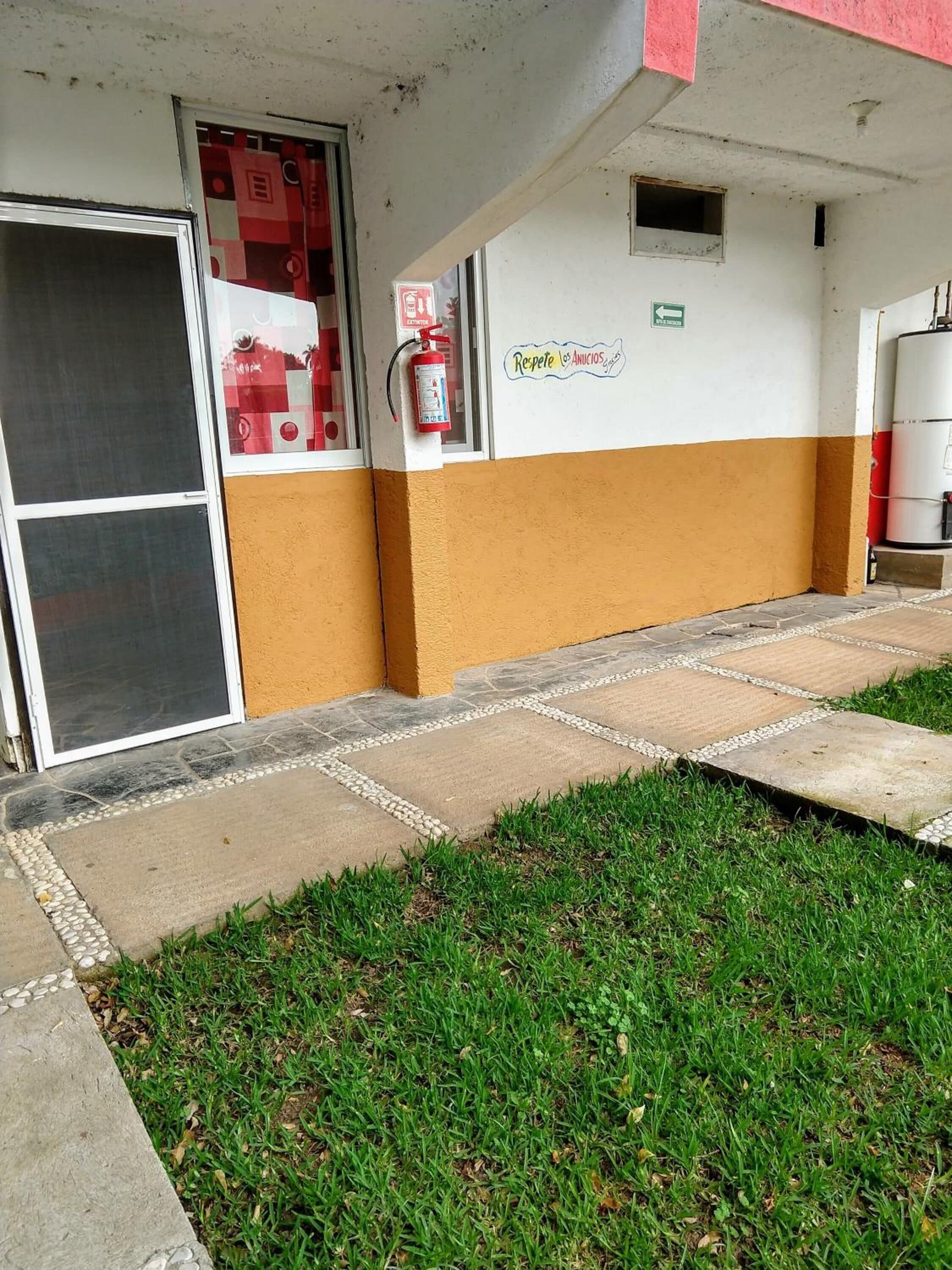 A building with a fire extinguisher mounted on the wall, a fire hose, and a sign that reads "Respete los Anuncios".