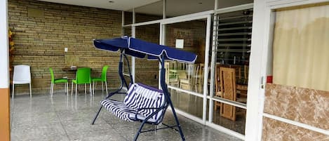 Un espacio de patio con una silla mecedora, sillas verdes y una mesa.