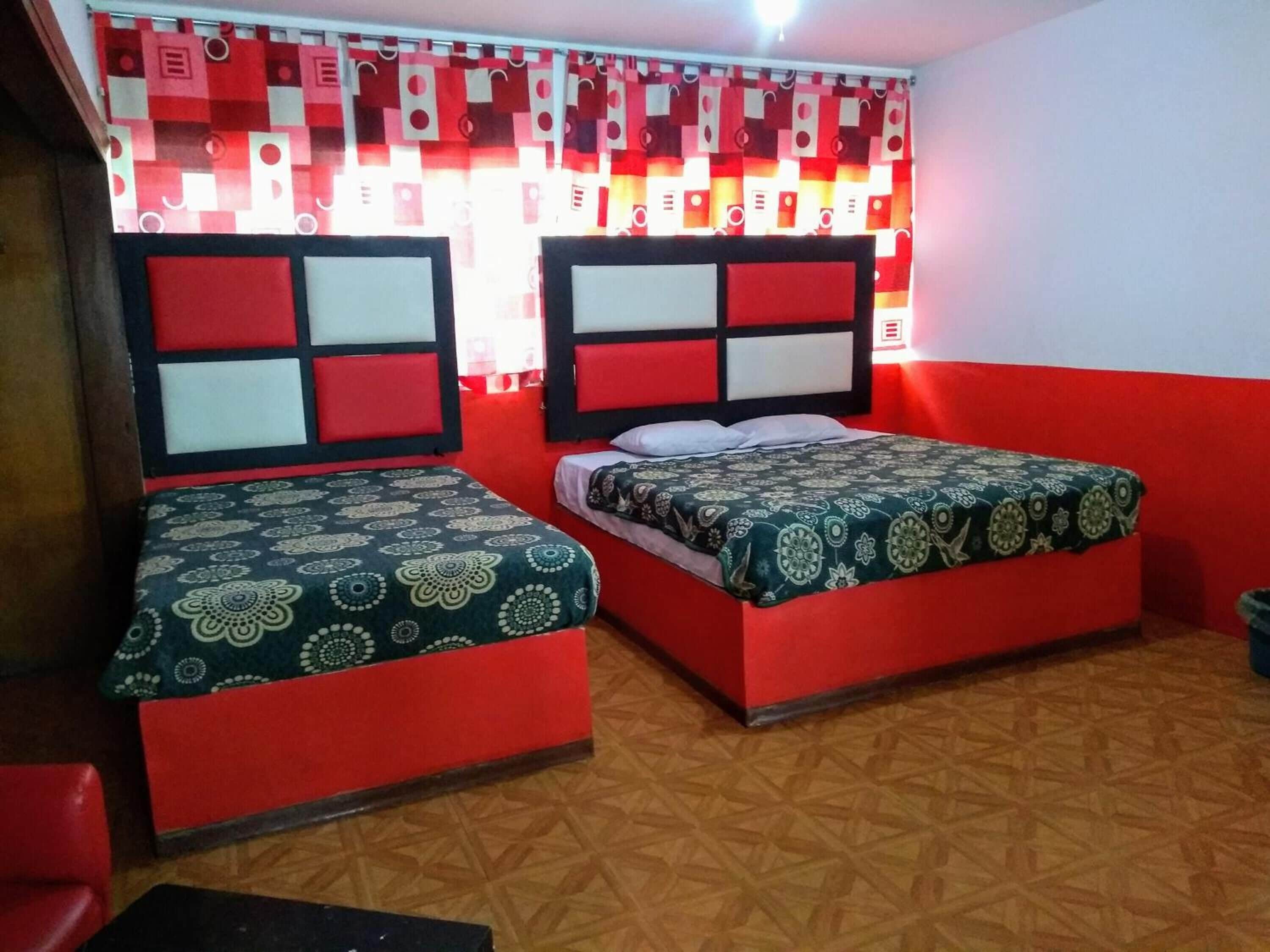 Una habitación con dos camas, cabeceros rojo y blanco, cubrecamas estampados y un suelo con diseño geométrico.