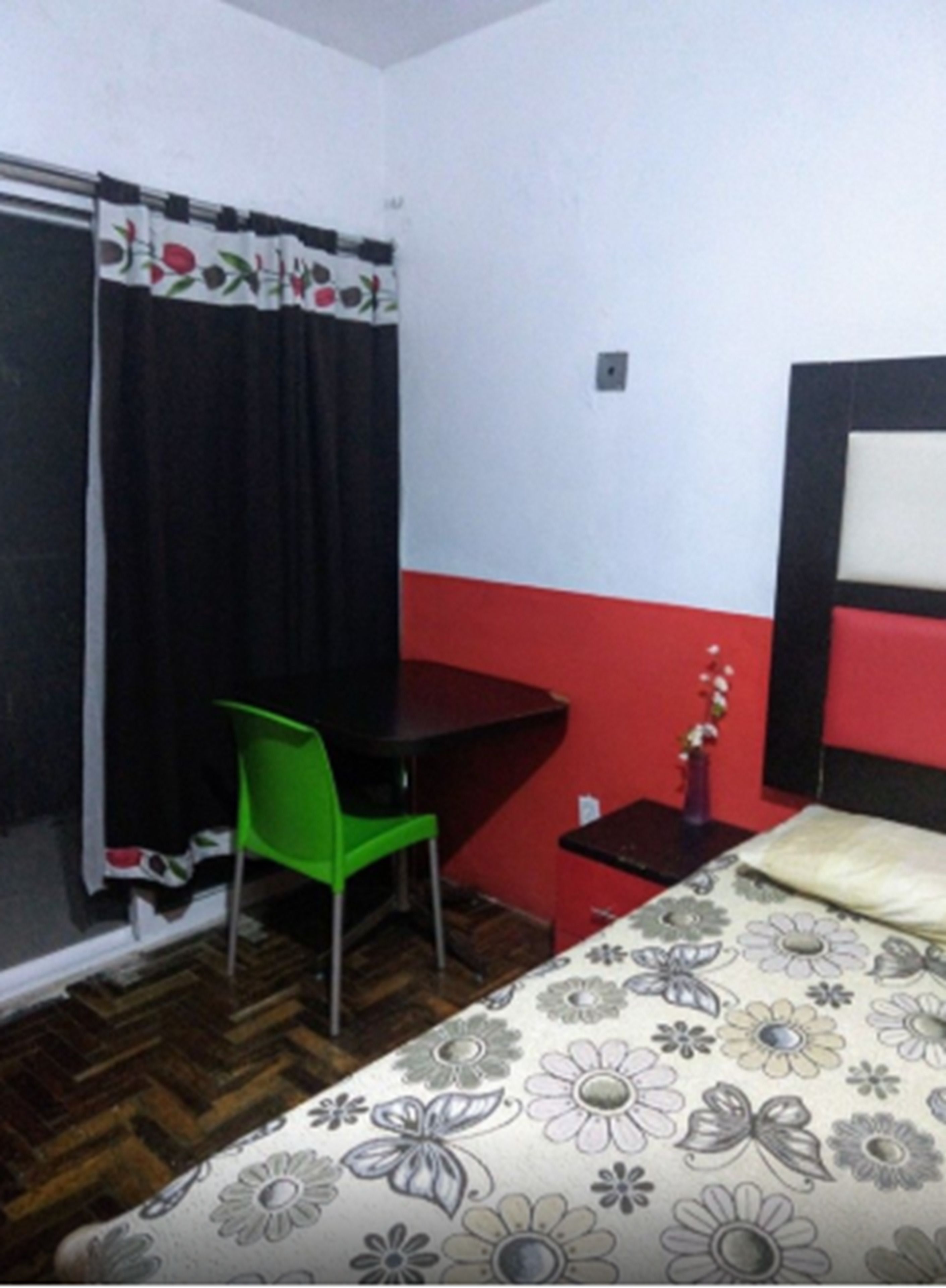 A room with a bed, a desk, a chair, and a small table with a vase.