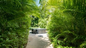 A pathway flanked by lush green foliage leading to a central water feature. - Luxe Tao Riviera Resort Condo w/ Beach & Golfing! (Solidaridad)