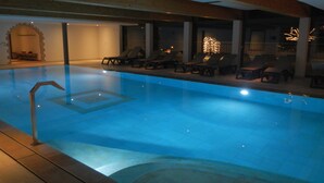 Une piscine entourée de chaises longues et de transats, le tout abrité par une zone couverte d’où l’on peut admirer le ciel nocturne.