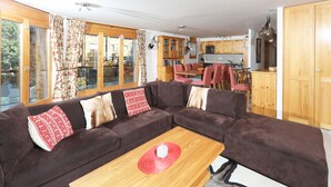 Un salon moderne avec un canapé d’angle marron, une table basse en bois et un coin cuisine doté de meubles en bois et d’une table à manger.