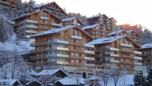 Un hôtel à plusieurs étages doté de balcons, d’une façade en bois et entouré d’un paysage enneigé.