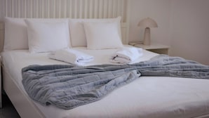 A neatly made bed with white linens and a gray quilt, a bedside lamp, and a white headboard.